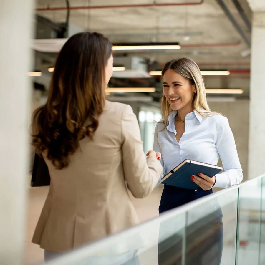 Two professional women shaking hands and smiling in a modern office setting